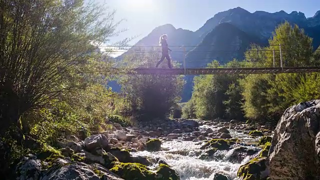 一名年轻女子正穿过山间溪流上的吊桥视频下载