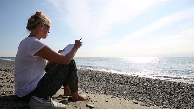一个女人在海滩上用写生本，眺望大海视频素材
