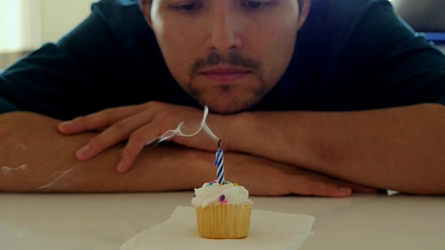 孤独的年轻人吹灭纸杯蛋糕上的生日蜡烛，做了一个悲伤的表情视频下载