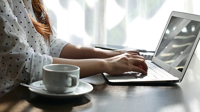 年轻女子在家里用笔记本电脑在木头桌子上工作视频下载