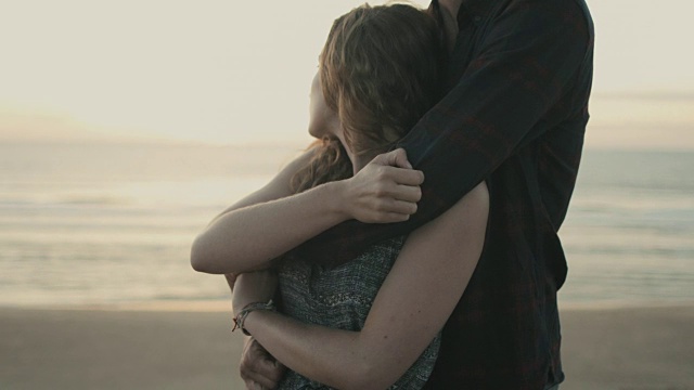 在法国南部的大西洋海滩上，一对相爱的年轻夫妇在一起享受时光，彼此紧紧地抱着，在沙丘上看日落视频素材