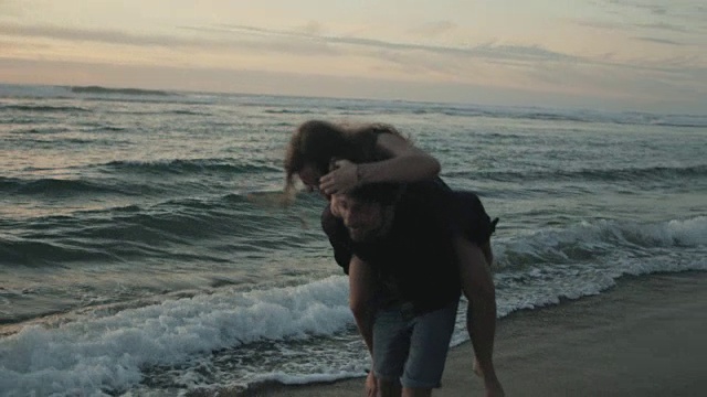 在法国南部的大西洋海滩上，一对相爱的年轻情侣在一起享受时光，在夕阳下玩水，背着背包视频素材