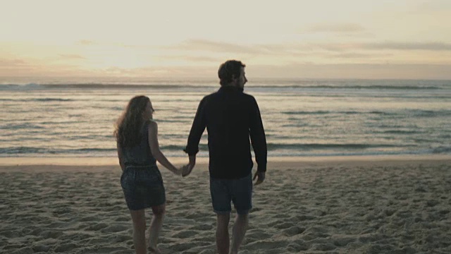 在法国南部的大西洋海滩上，一对相爱的年轻夫妇在一起享受时间，朝着夕阳下的海水走去视频素材