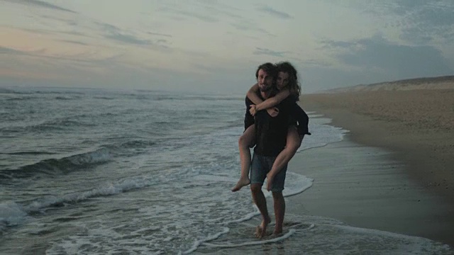 在法国南部大西洋的一个荒芜的海滩上，一对相爱的年轻情侣在一起享受时光，背着背包，在夕阳下玩水视频素材