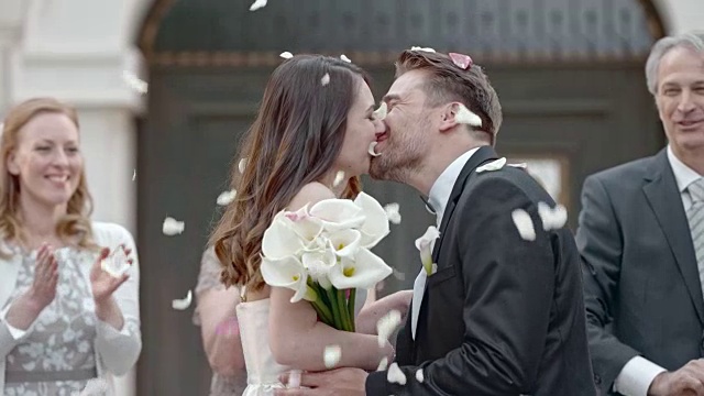 婚礼宾客向亲吻的新婚夫妇投掷花瓣视频下载