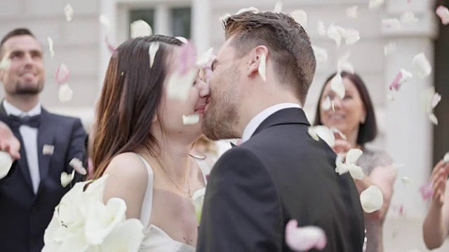 新婚夫妇亲吻，而婚礼上的客人扔花瓣视频素材