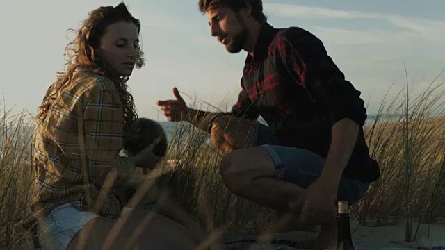 在法国南部大西洋海滩的沙丘上，一对相爱的年轻夫妇准备野餐，在沙滩上的野餐毯子上放着西瓜和葡萄酒视频下载