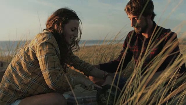 在法国南部的大西洋海滩上，一对相爱的年轻夫妇在一起享受时光，在沙滩上搭起野餐毯，切西瓜视频素材