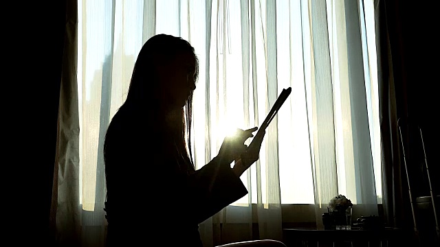 日落时分，女商人在窗边使用平板电脑。视频素材