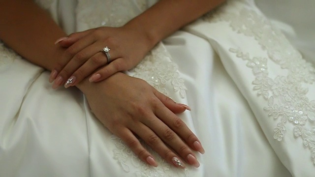 穿着白色礼服的新娘坐在床上，手指上戴着结婚戒指视频下载