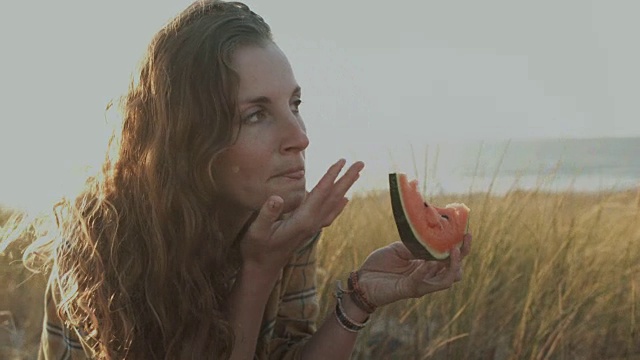 美丽的女人在阳光下吃西瓜在沙滩沙丘在大西洋在法国南部视频素材