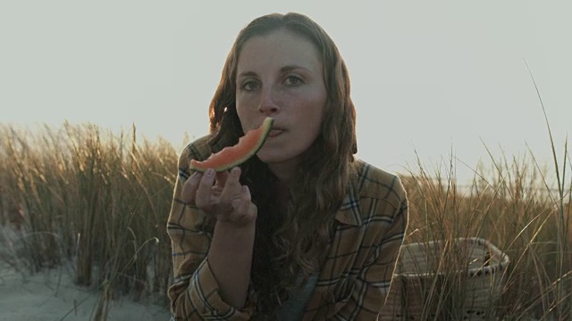 美丽的年轻女子的肖像，吃西瓜，看着相机，笑，开玩笑在沙丘上的大西洋海滩在法国南部视频素材