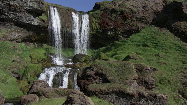 中等镜头的瀑布流到悬崖上的苔藓覆盖的岩石视频素材