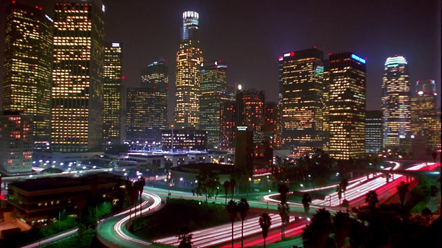 高角度广角拍摄的时间推移高速公路上的交通与办公大楼照亮了背景/白天到晚上/加州洛杉矶视频素材