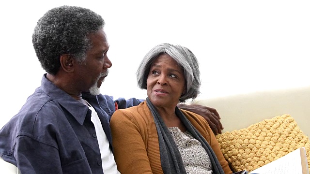高级非裔美国人夫妇在沙发上微笑和大笑视频素材