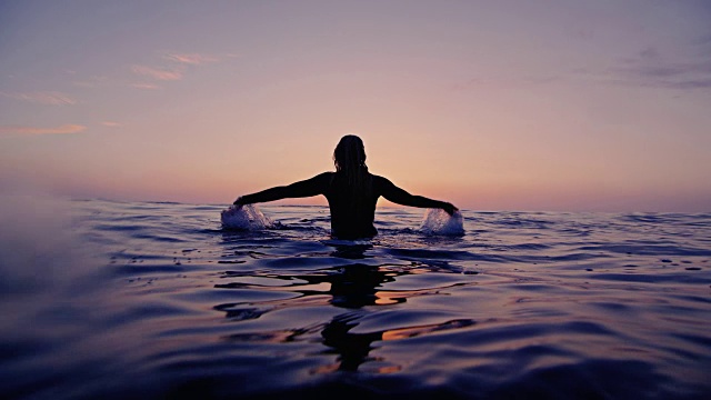冲浪女孩溅水在一个加利福尼亚的晚上，而坐在冲浪板拍摄在日落的慢动作。视频素材