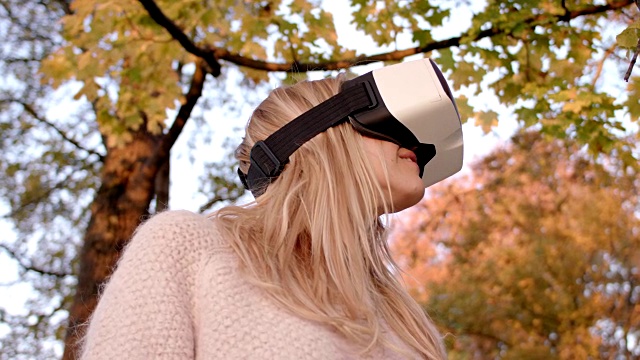美丽的女人在她的30多岁与金色长发/使用虚拟现实眼镜在秋天的树前/拍摄1视频下载