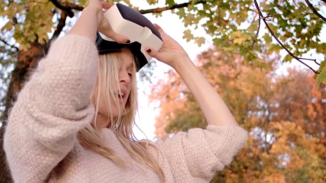 美丽的女人在她的30多岁与金色长发/使用虚拟现实眼镜在秋天的树前/ shot-2视频下载