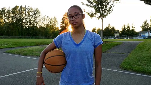 一个年轻女子在夏天的晚上拿着篮球的肖像视频下载