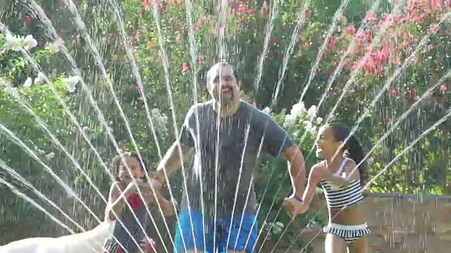 父亲与2个女儿在洒水器中玩耍视频下载