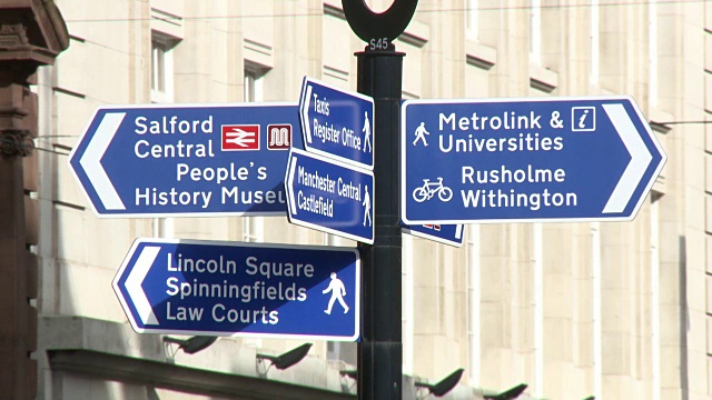 一个蓝色路标的特写，在曼彻斯特中心指示Rusholme, Withington, Salford, Lincoln广场，Spinningfields，人民历史博物馆和法院，英国。视频下载