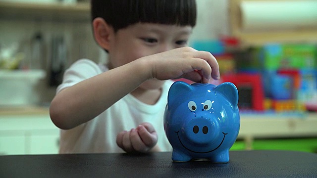 小男孩把一枚硬币放进扑满——孩子为未来存钱的概念视频下载