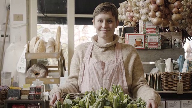 店员提着一个装着有机花椰菜的篮子进了店，对着相机微笑，然后走出相框。视频素材