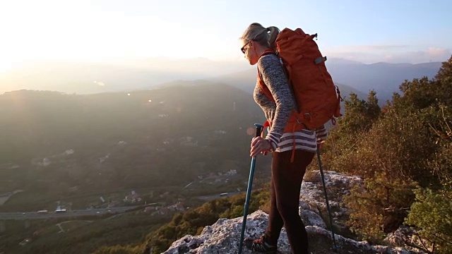 女徒步者爬上岩架，远处的山丘，日出视频素材