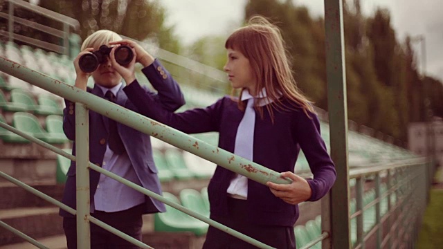 一个十来岁的小女孩用双筒望远镜看向别处，弟弟在旁边，侧面视频下载