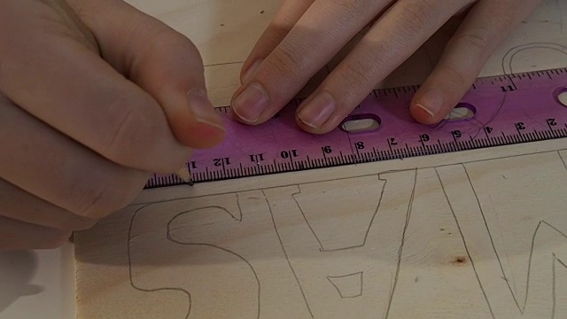 特写的女孩的手做工艺品。她正在用尺子在一块木板上画一个正方形。在木板上写着圣诞节。视频素材