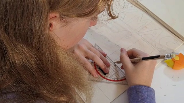 高瞻远望的女孩(13-14岁)做工艺品。她在木板上借助一个角度传送带画线。它´s写圣诞。视频素材