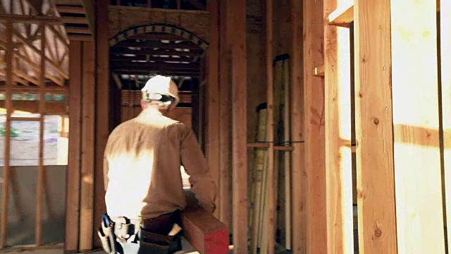 一名成年男子扛着一块木板穿过建筑工地。视频素材