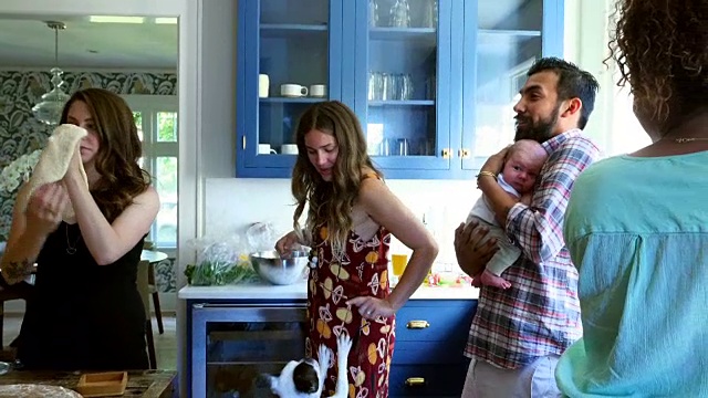 在厨房和朋友准备晚餐时，一名男子抱着刚出生的婴儿为朋友视频下载