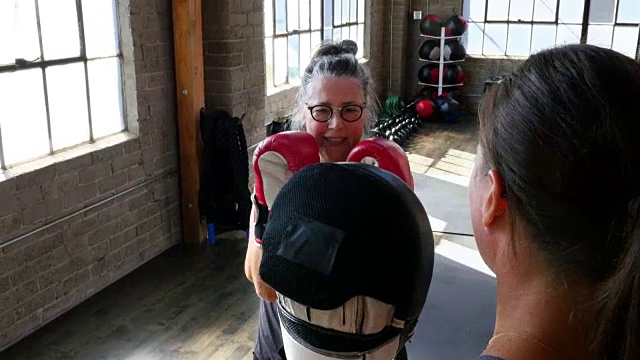 笑着的成熟女人在健身房和教练拳击视频下载