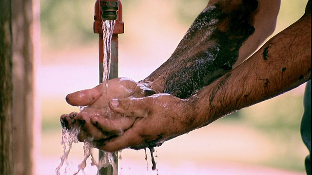慢镜头近距离拍摄在爱荷华州的户外水龙头下，一名男子正在清洗双手和手臂上的黑色油脂和污垢视频素材