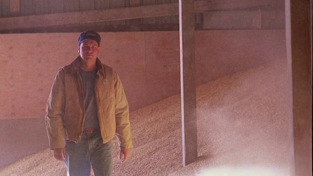 慢动作中镜头男子走向相机旁边的谷物堆和擦灰尘从夹克袖子/爱荷华视频素材