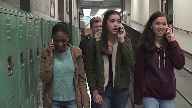 三个朋友在学校走廊里打电话的中间镜头视频素材