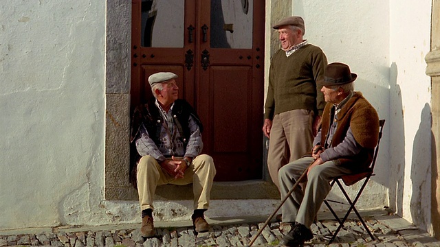 (宽镜头)葡萄牙蒙萨拉兹村街道的一边，三个高级男子在隔壁交谈视频素材