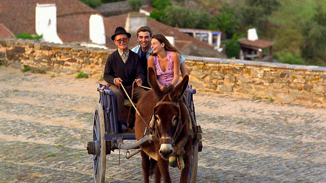 高角度广角拍摄，老人驾驶驴车年轻的游客夫妇在村庄道路/蒙萨拉兹，葡萄牙视频素材