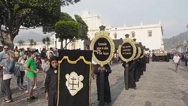 大斋节/复活节庆典期间，安提瓜瓜瓜大教堂前的天主教游行。人们穿着黑色服装，举着写有《圣经》信息的横幅。视频下载