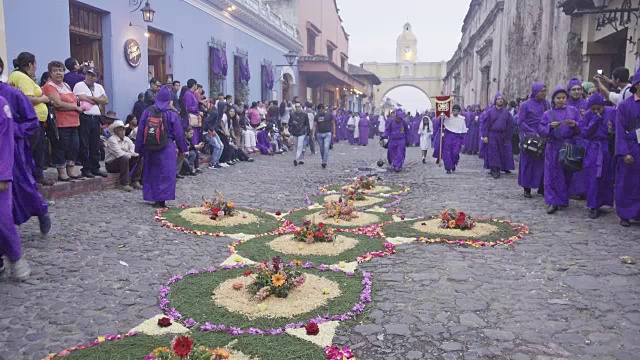 在危地马拉安提瓜举行的大斋节/复活节天主教庆典。鹅卵石街道上铺着五颜六色的花毯。人们穿着紫色的服装穿过圣卡塔琳娜拱门。视频下载