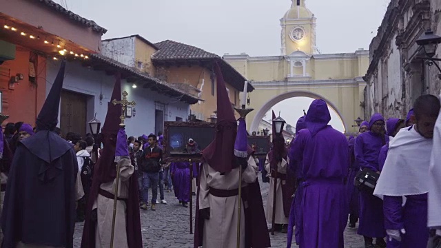 在大斋节/复活节庆祝期间，危地马拉著名街道安提瓜的天主教游行。人们穿着紫色的服装，戴着头巾穿过圣卡塔琳娜拱门视频下载