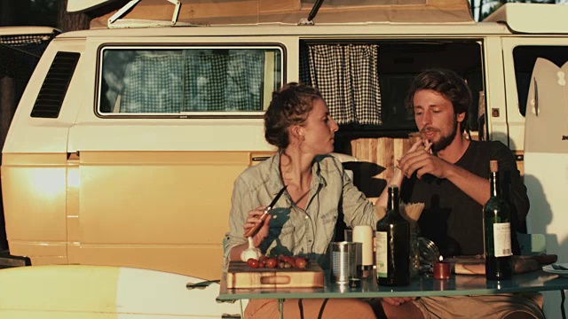 在法国南部的露营地，一对相爱的年轻情侣一起享受时光，在日落时分在大众汽车前准备晚餐，调情，品尝，切蔬菜。视频下载