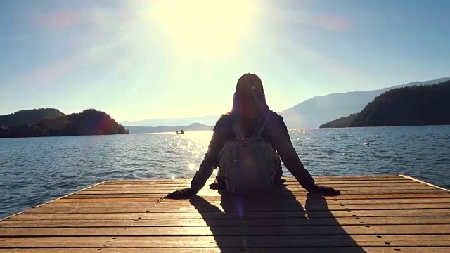 年轻女子坐在湖边的码头上休息视频素材