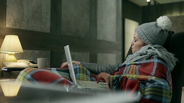 年轻女子用毯子盖着电脑和手机视频下载