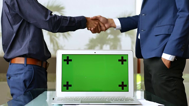 两个商人在绿色屏幕的笔记本电脑后面握手视频下载