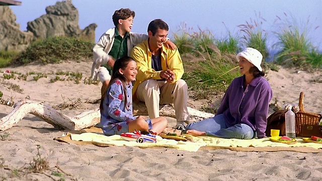 一家人坐在沙滩上的毯子上，女孩在吃西瓜/加州视频素材