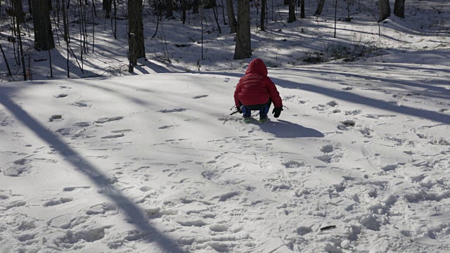 蹒跚学步的小男孩用棍子在雪地里画画视频素材