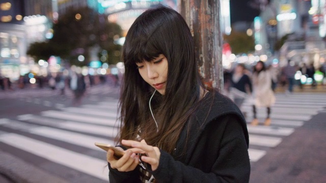 日本东京，一位年轻的日本女子一边听音乐一边查看手机视频素材