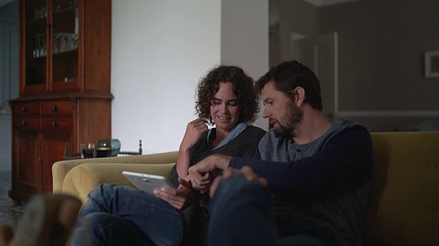 一对幸福的夫妇在家里的沙发上使用数码平板电脑视频素材
